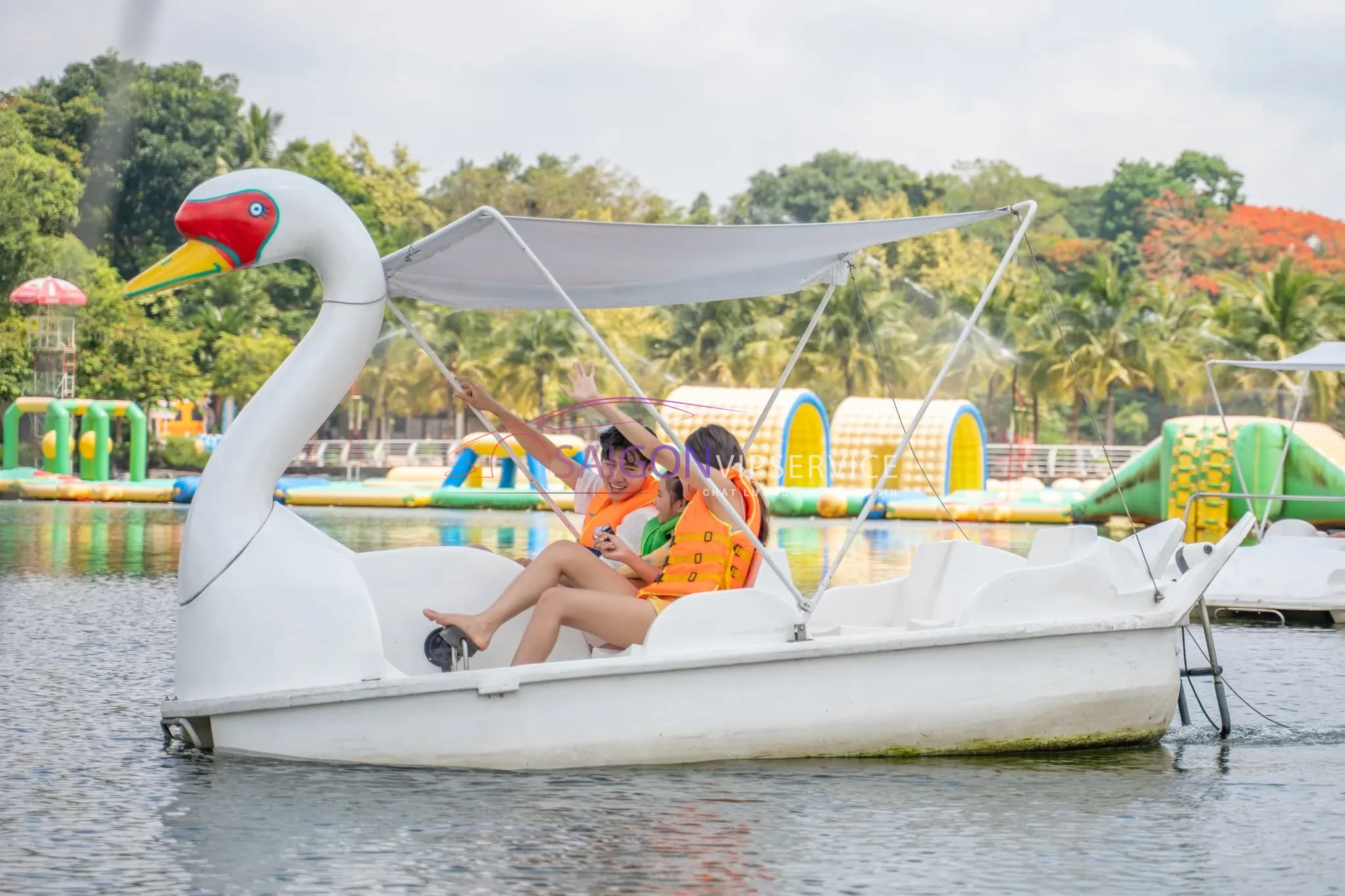 Hai du khách mặc áo phao đang vui vẻ trải nghiệm trò chơi đạp vịt thiên nga trên mặt hồ trong xanh tại Suối Mơ.