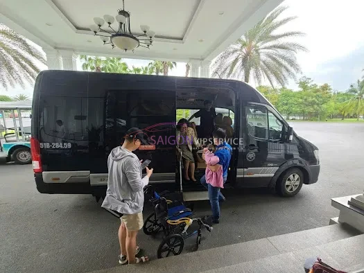 Nhóm hành khách đang bước lên chiếc xe du lịch màu đen hiện đại được đỗ ngay trước sảnh lớn của một resort